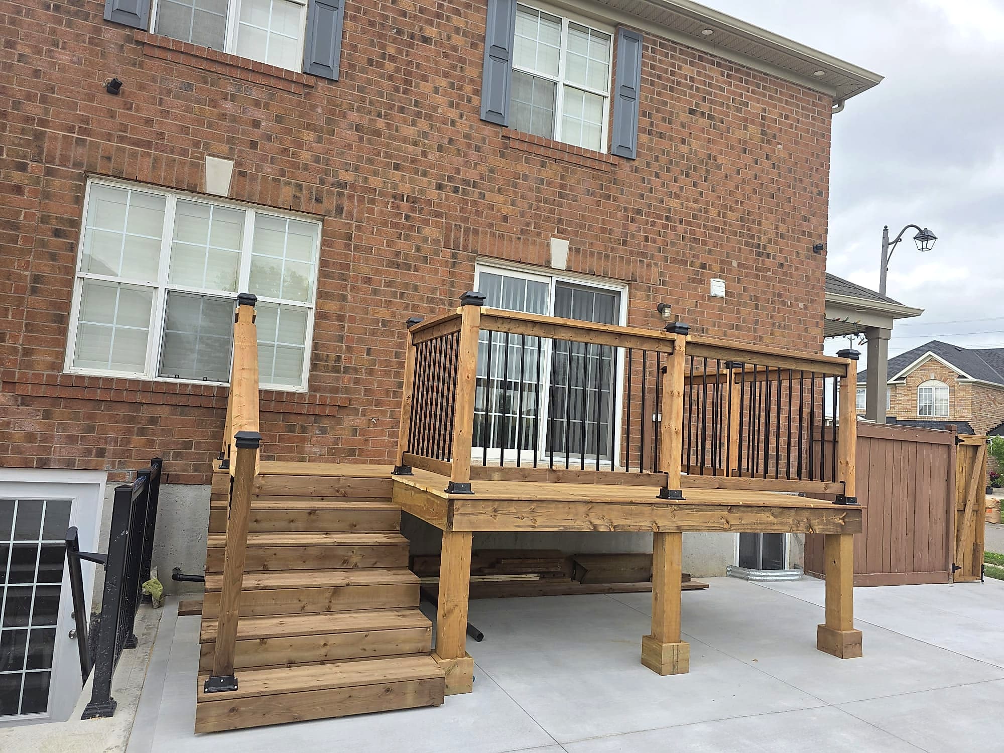 Raised deck with black aluminium spindle railing and a wide stair run onto a concrete pad