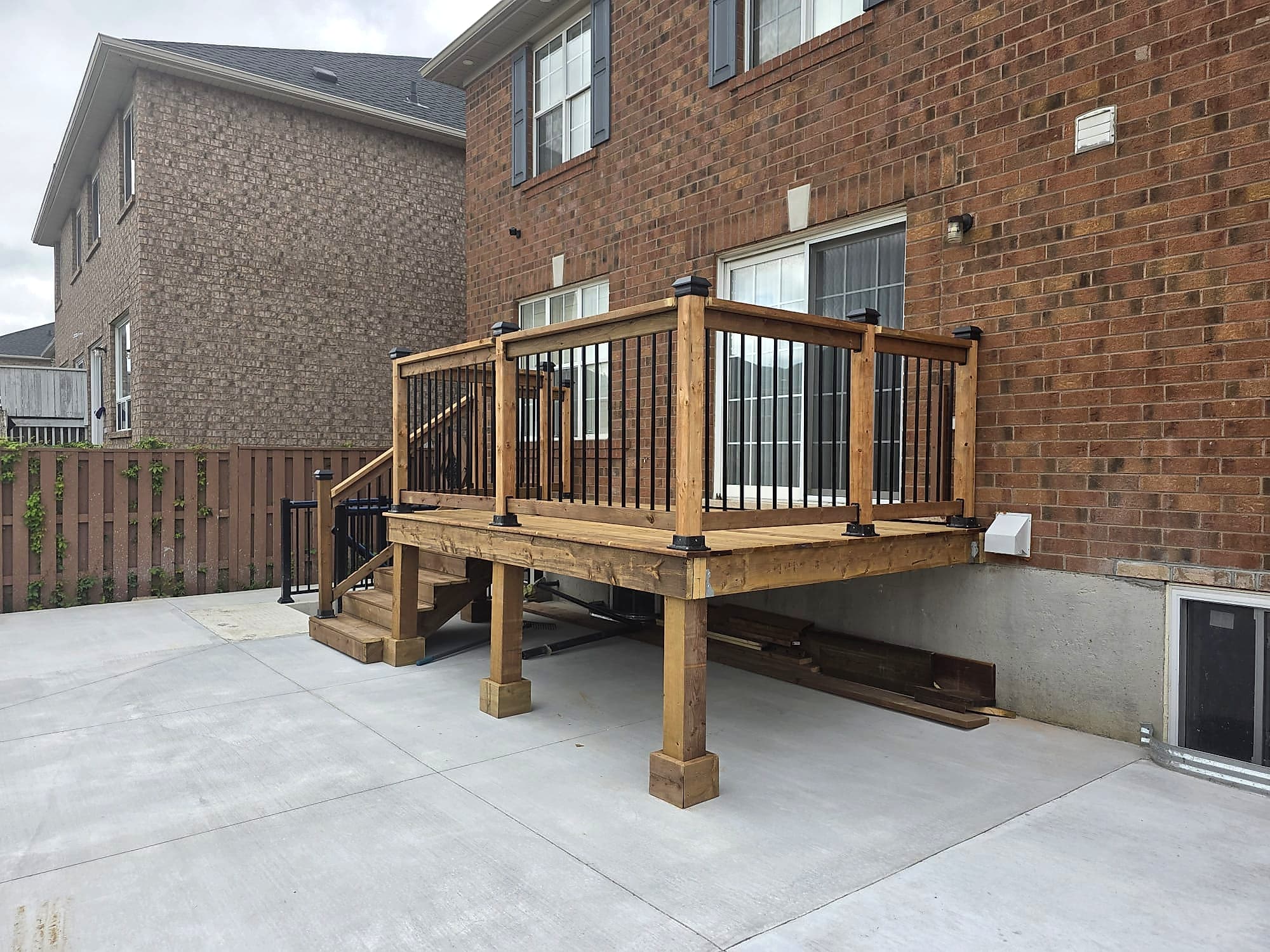 Corner view of a raised pressure-treated deck on wrapped posts with black aluminium spindle railing