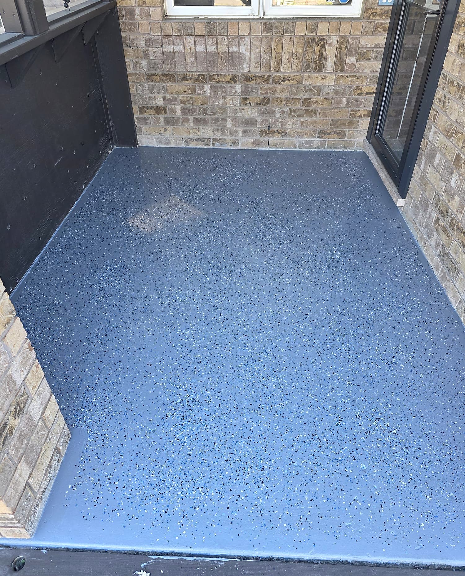 Covered porch floor finished in grey epoxy flake coating with a coved edge up to the brick