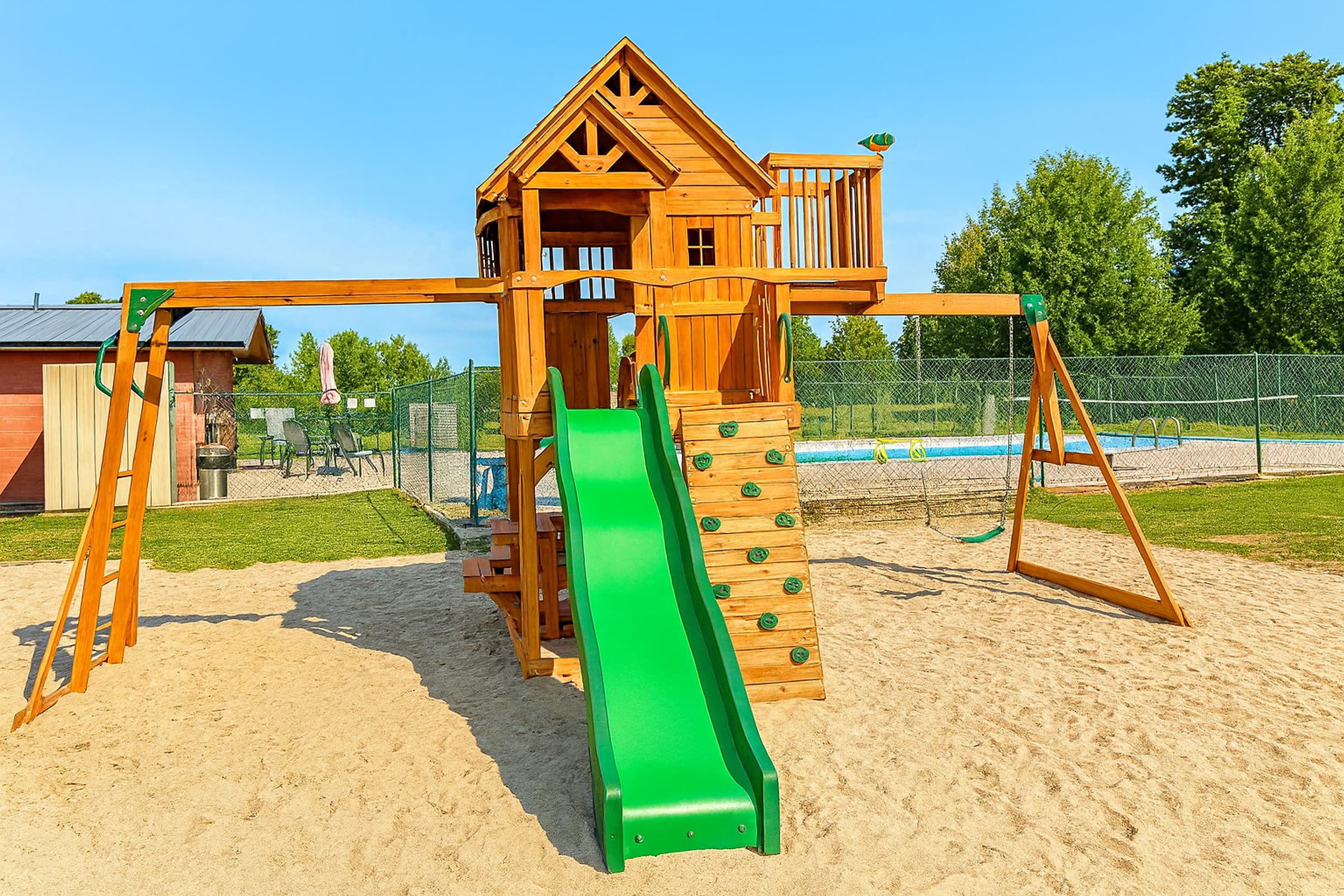 Cedar play structure with a gabled playhouse, green slide, climbing wall and swing beams set in a sand base
